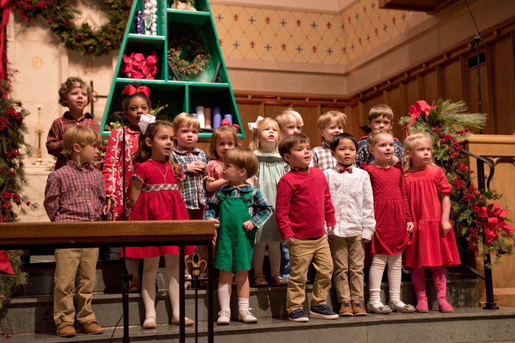 group of small children singing, dressed in festive clothes standing on chancel stairs with holiday garland around.
