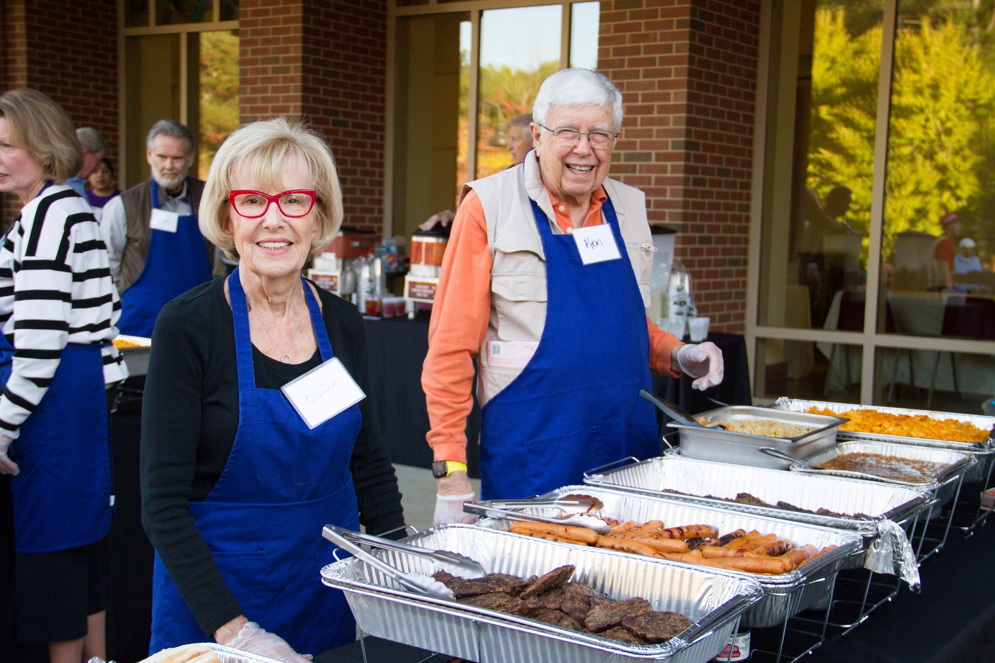 man and woman wearing aprons smiling and serving food